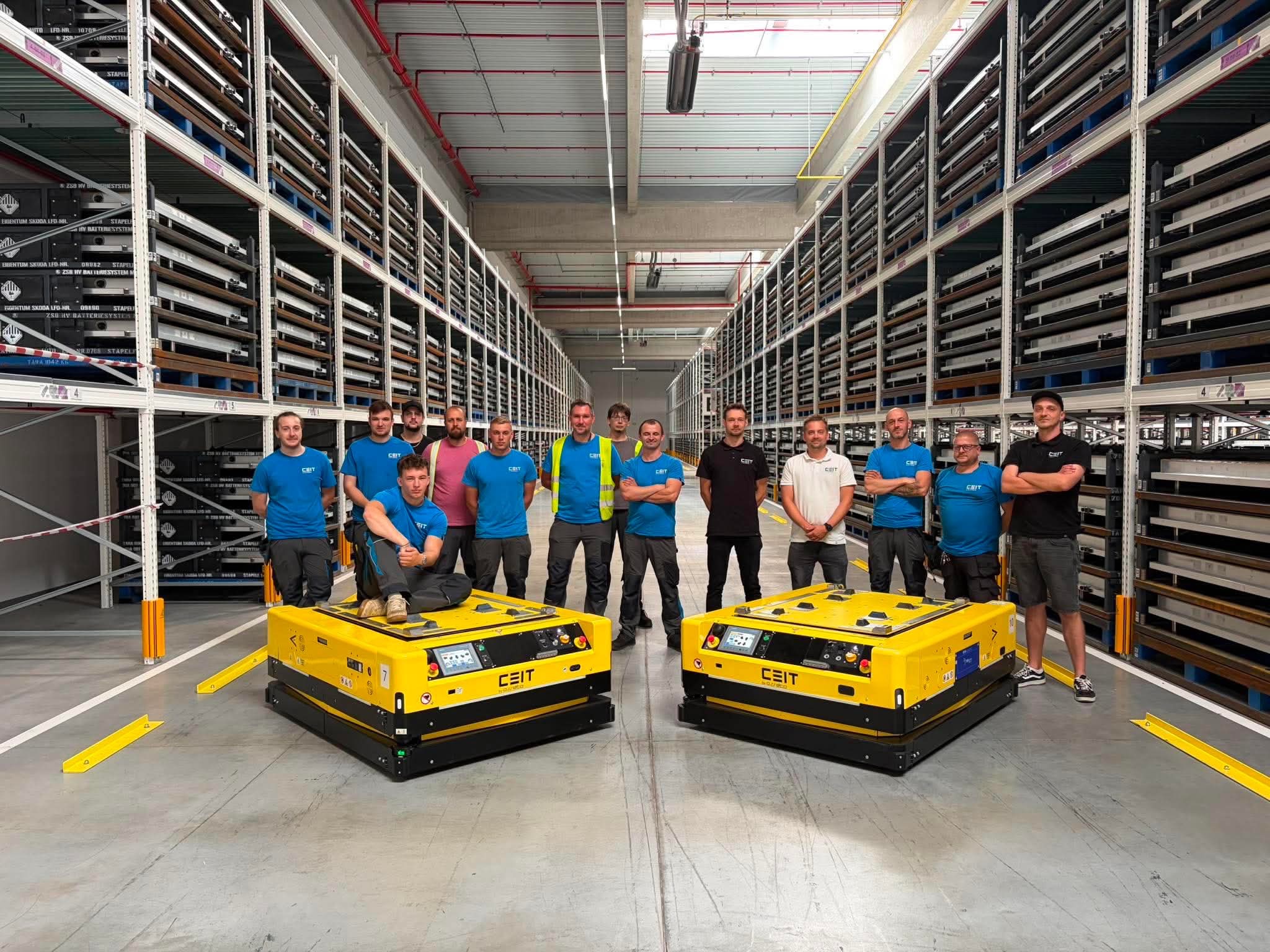 Tým Asseco CEIT se dvěma žlutými autonomními mobilními roboty ve skladové hale